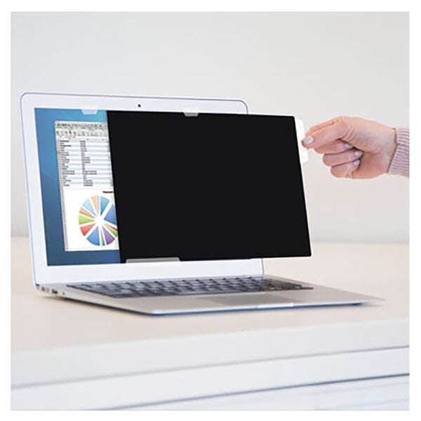 A hand holding a Fellowes PrivaScreen black privacy filter over a laptop screen.