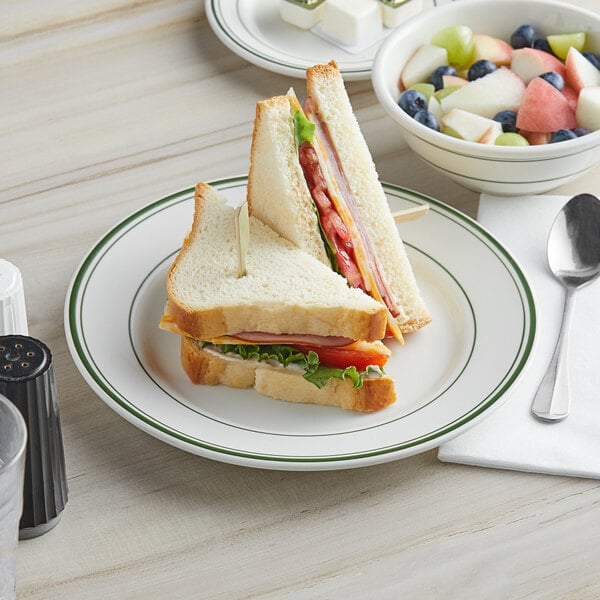 A Tuxton Green Bay Ivory china plate with a sandwich and fruit.