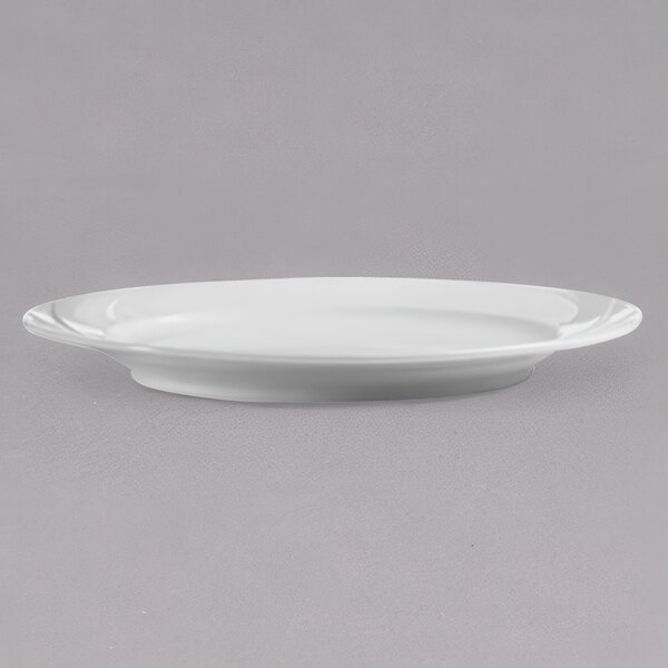 An Arcoroc white porcelain dinner plate with a rim on a gray surface.