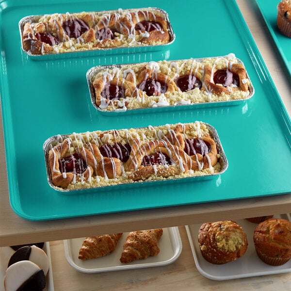 A green Cambro market tray with pastries and muffins on a bakery display.