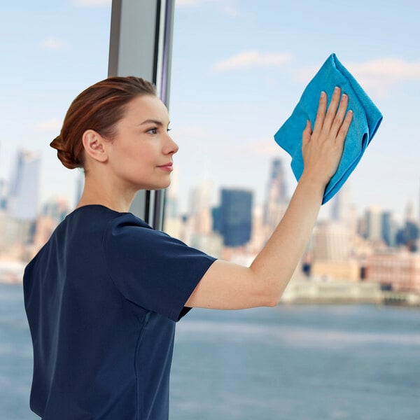 A person cleaning a window with a blue Rubbermaid HYGEN r-40 16" x 16" recycled microfiber cloth.
