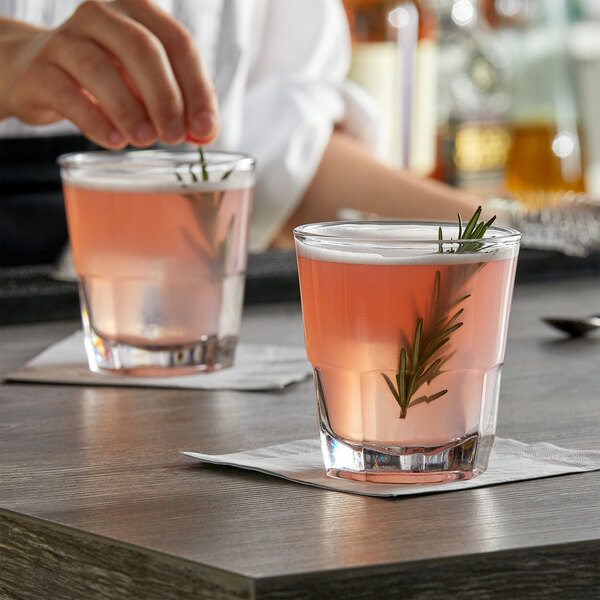 A person pouring a pink drink into an Anchor Hocking New Orleans Old Fashioned glass on a table.