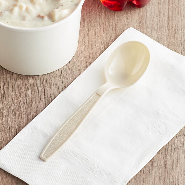 A Visions beige plastic soup spoon on a napkin next to a white bowl of soup.