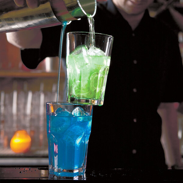 A bartender pouring a drink into an Arcoroc double old fashioned glass filled with ice.