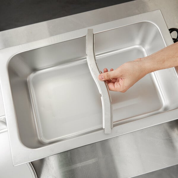 A hand using a Vollrath adapter bar to hold stainless steel containers over a sink.