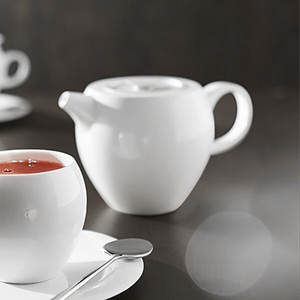 A white Chef & Sommelier bone china teapot with a lid and a cup of tea on a white plate.