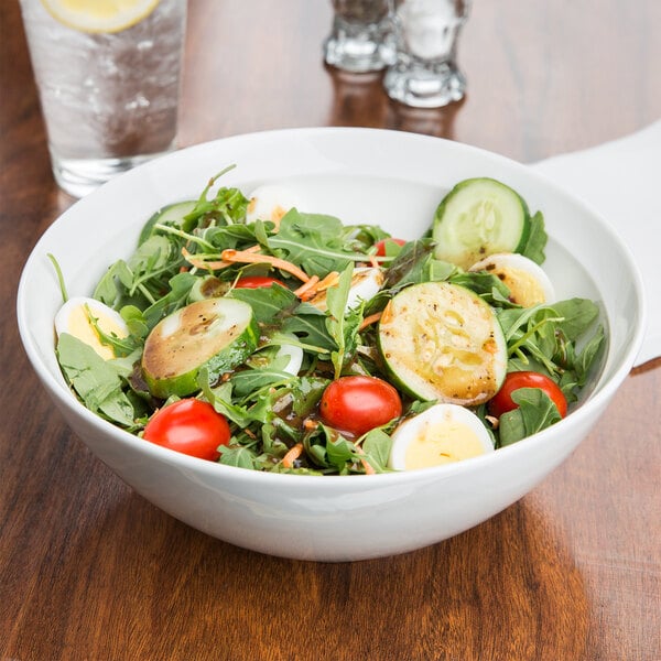 An Arcoroc serving bowl filled with salad with tomatoes, cucumbers, and other vegetables.