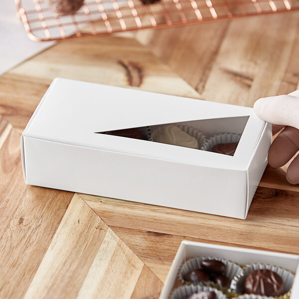 A person holding a white 1 lb. candy box with a triangular window containing chocolates.