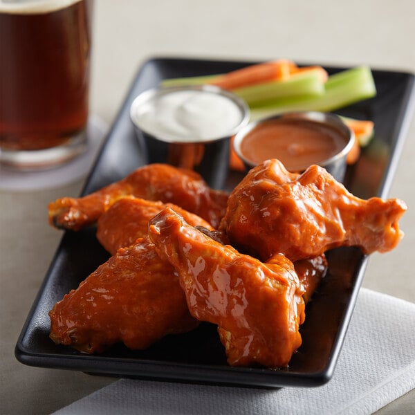 A plate of buffalo chicken wings coated in hot sauce, served with celery, carrot sticks, and dipping sauces.