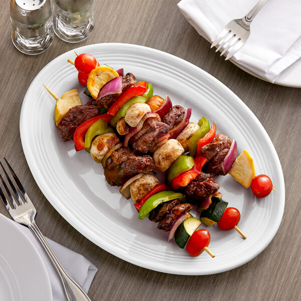 A plate of meat and vegetables on a Tuxton white oval china platter on a table.