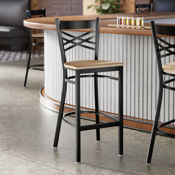 A black metal bar stool with a cross back design and a driftwood-colored wooden seat.