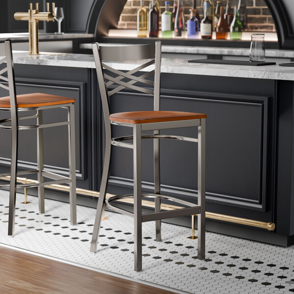 A metal bar stool with a cross back design and an antique walnut wood seat.