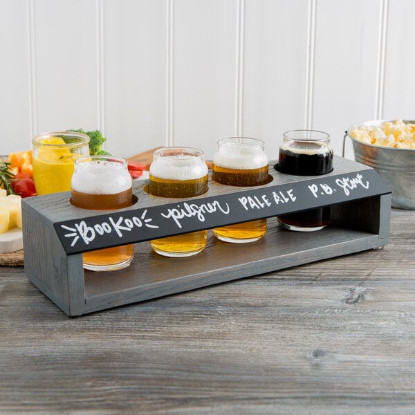 A Cal-Mil gray wood tasting caddy with four glasses of beer on a table.