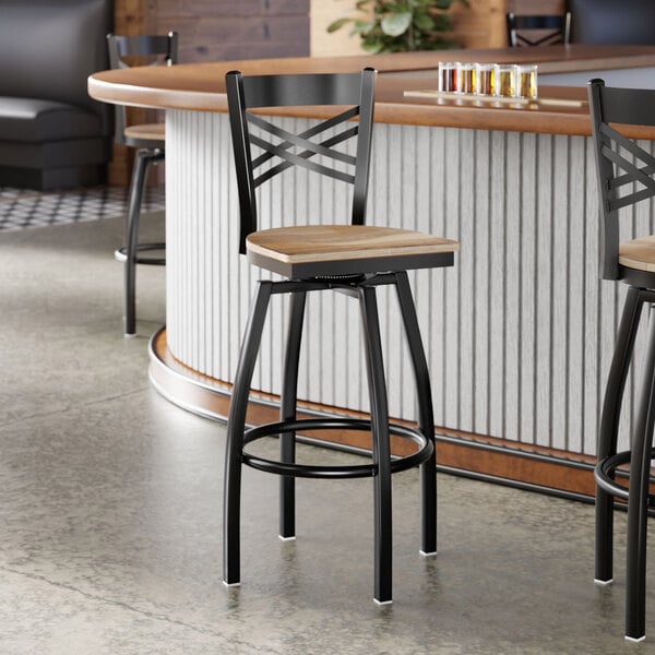 A black metal cross back swivel bar stool with a driftwood-colored wooden seat.