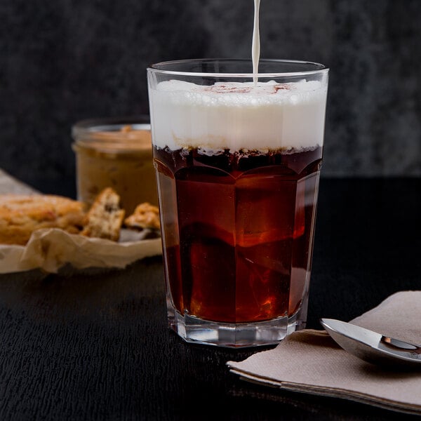 An Arcoroc Gotham beverage glass filled with brown liquid and white foam.