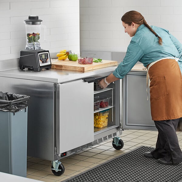 A woman in an apron using a Beverage-Air worktop freezer in a kitchen.