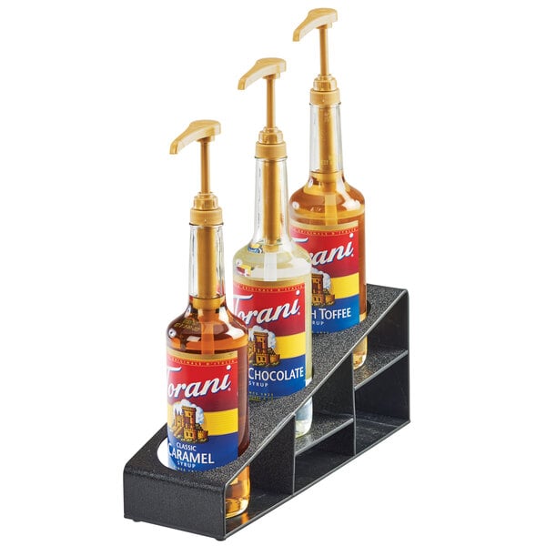 A black Cal-Mil 3 tier bottle organizer holding three bottles of liquid.