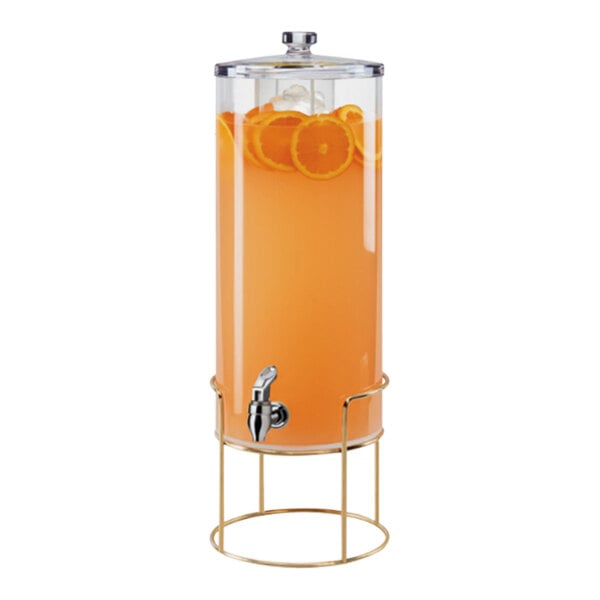 A Cal-Mil round glass beverage dispenser with an infusion chamber and brass wire base filled with orange juice.