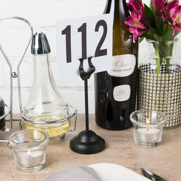 A black American Metalcraft harp table card holder with a number and flowers on a table.