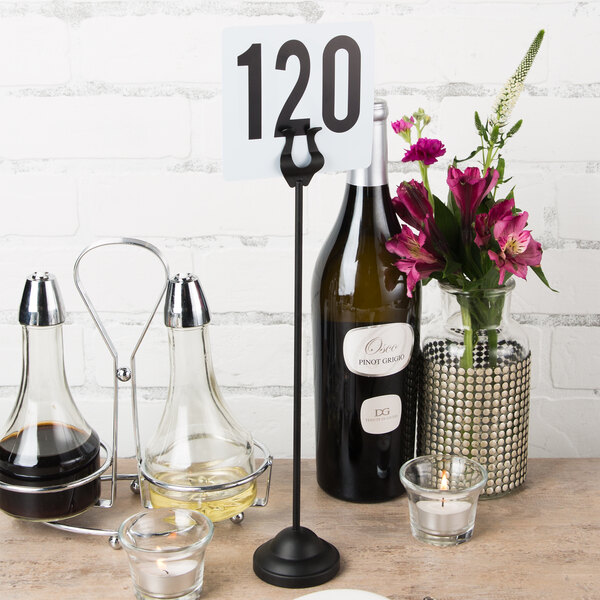 A black American Metalcraft harp card holder on a table with a number and flowers.