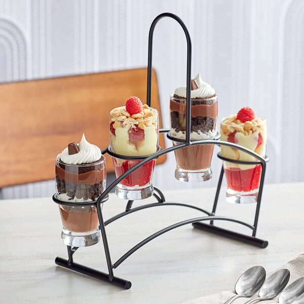 A black metal flight carrier holding Barbary tasting glasses on a table with desserts.