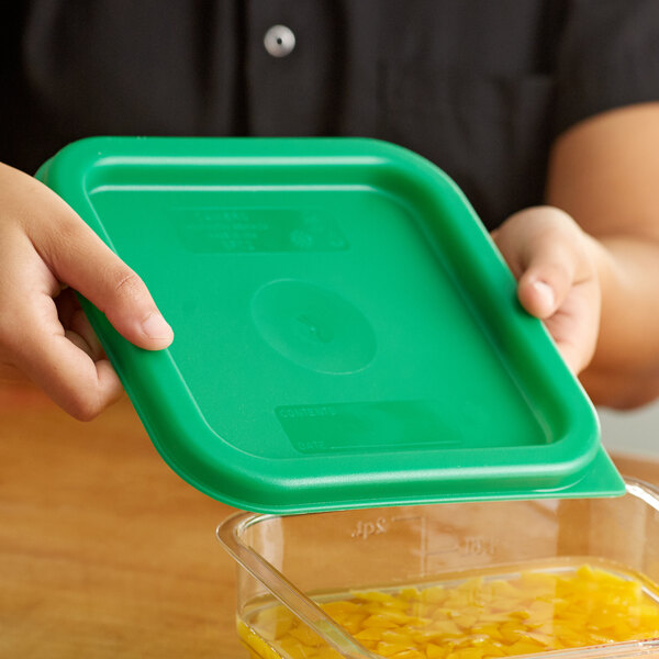 A person holding a green lid over a plastic container of food.