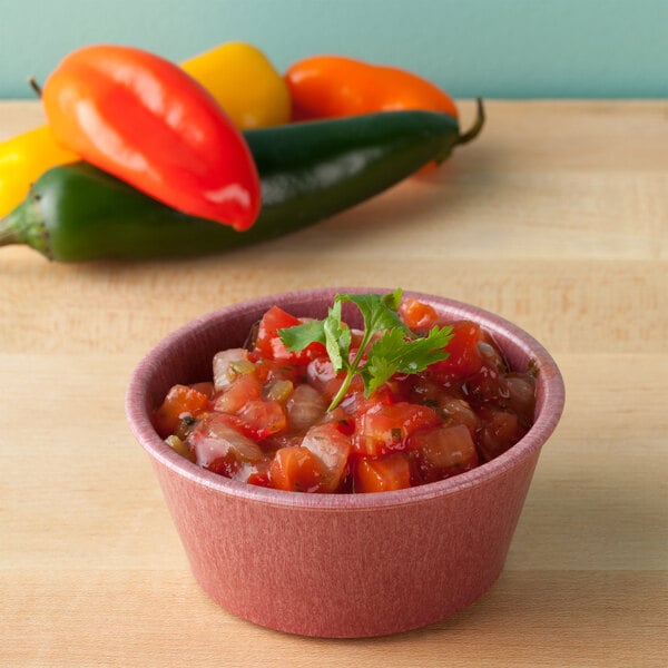 A raspberry ramekin filled with salsa on a table.