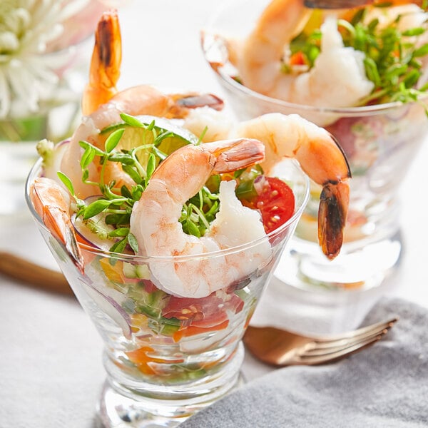 An appetizer of jumbo shrimp in a cocktail glass with tomatoes, herbs, and lime