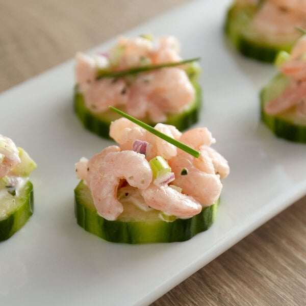 A plate of hors d'oeuvres with tiny sized shrimp on top of cucumber slices