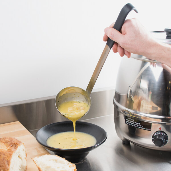 A person using a Vollrath stainless steel ladle to pour soup into a bowl.