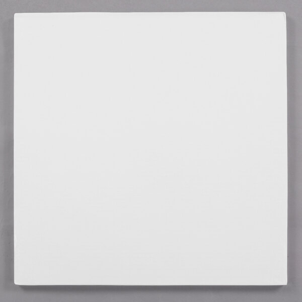 A white square Enjay cake drum on a gray surface.