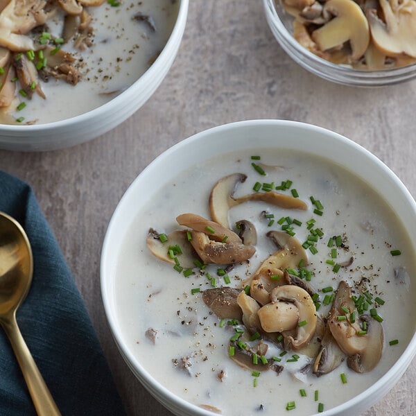 A bowl of soup with mushrooms and green onions served with a spoon.