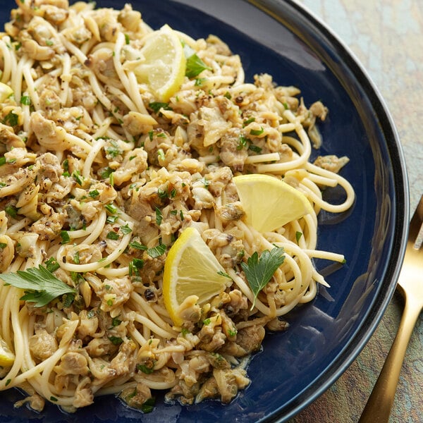 A blue plate of pasta with Martel baby clams, lemon slices, and parsley.