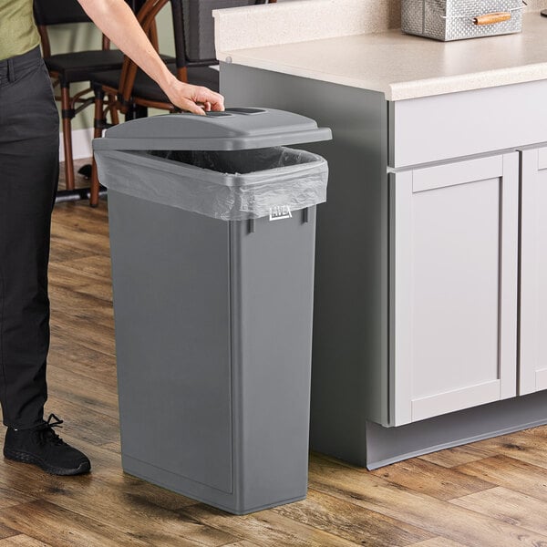 A person standing next to a Lavex gray slim rectangular trash can.