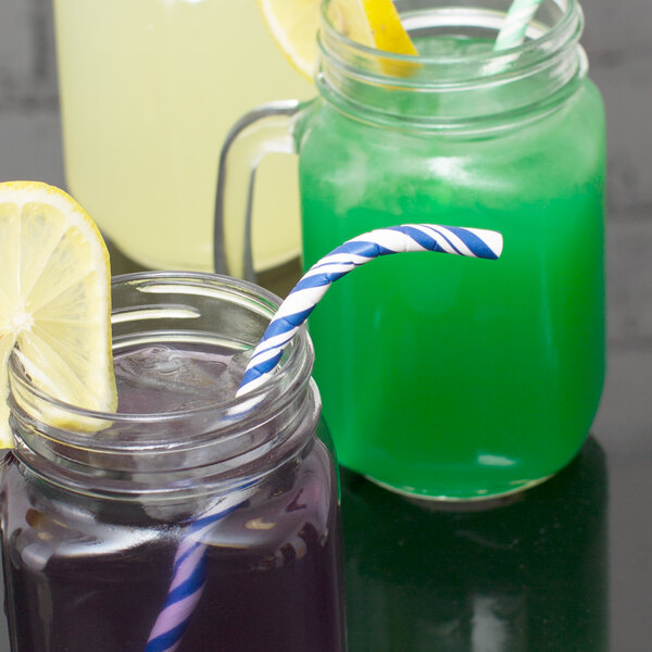 A glass jar with a blue and white striped straw and a green liquid with a lemon slice in it.