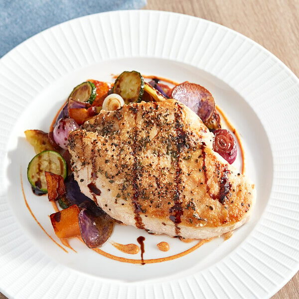 A white plate of Mountaire Farms boneless skinless chicken breasts and vegetables on a wood table.