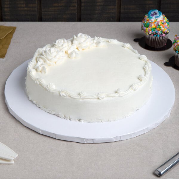 A plain white round cake with minimal floral decorations on top, displayed on a thick white cake drum.