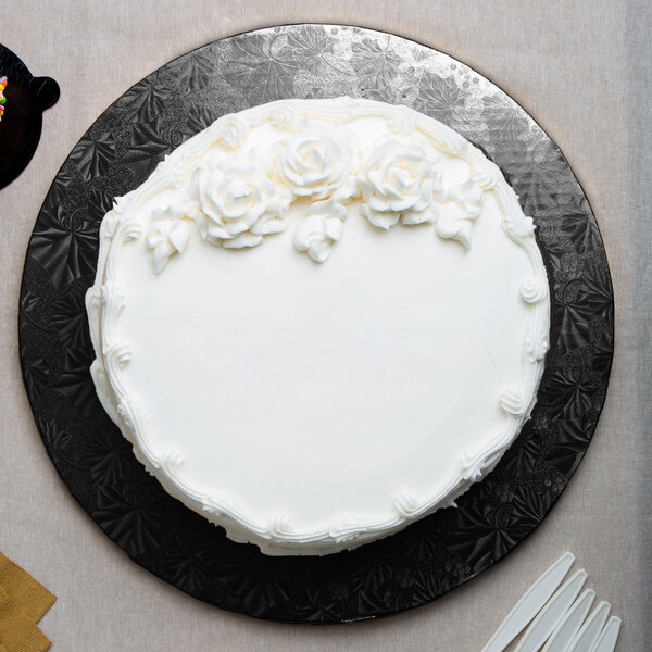 A white cake with white frosting and flowers on a black Enjay round cake drum.