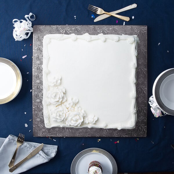 A white square cake on a black Enjay cake drum with silverware.