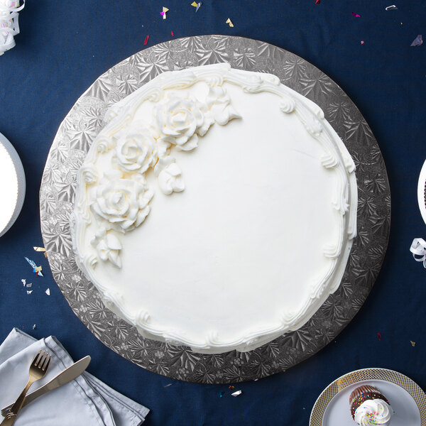 A white cake on a black Enjay round cake drum with white frosting and flowers.