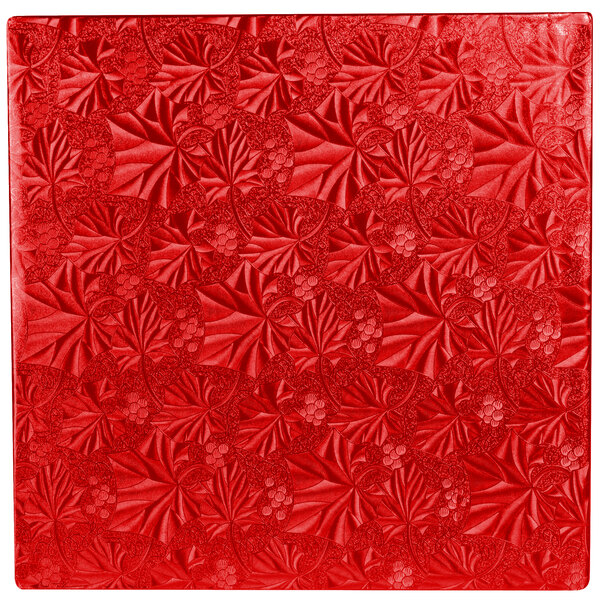 A white square cake drum with a red surface and floral designs.