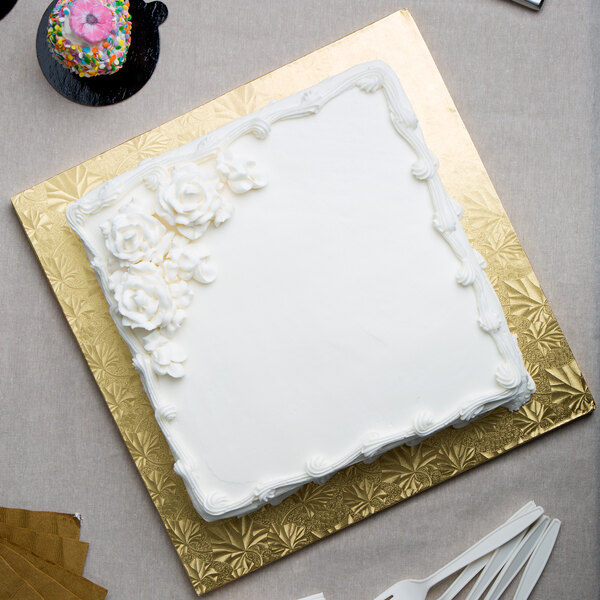 A white cake with frosting and flowers on a gold Enjay square cake drum.