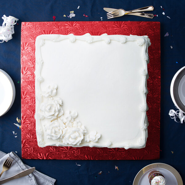 A white cake with white frosting on a red Enjay square cake drum.