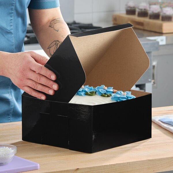A black cake or bakery box with a partially open lid, containing a decorated cake inside.