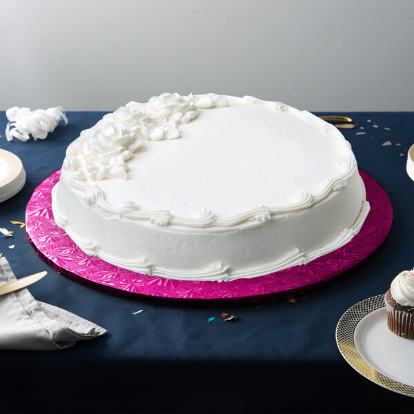 A white cake with pink frosting on a pink Enjay cake board on a table.