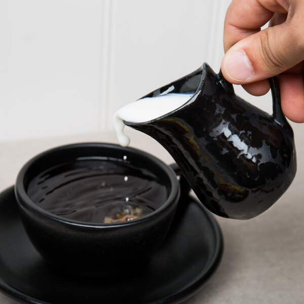 A person pouring milk into a black American Metalcraft porcelain bell creamer.