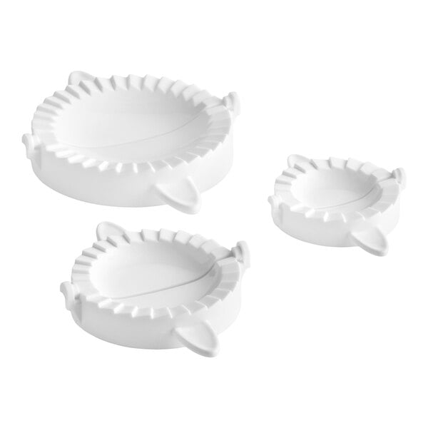 A set of three white plastic dumpling or pierogi presses in different sizes.