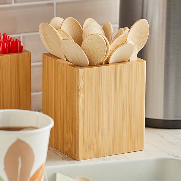 An American Metalcraft bamboo wood caddy holding wooden spoons and cups on a white counter.