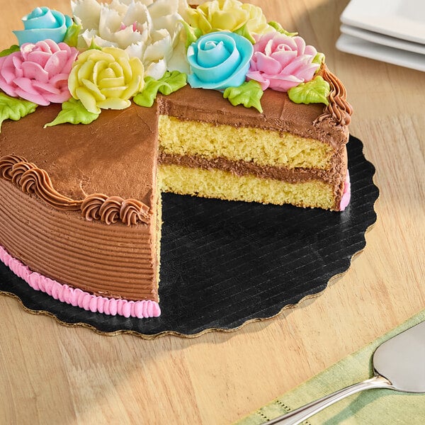 A black Enjay laminated corrugated cake circle with a chocolate cake with flowers on top on a table.