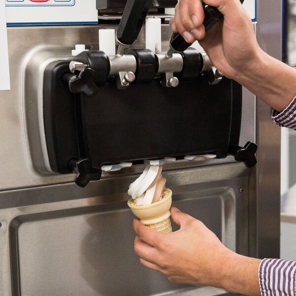 Person dispensing chocolate and vanilla swirled soft serve ice cream into cake cone